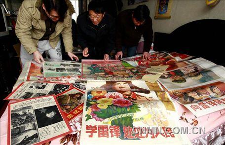 3月1日，房冠龍（中）在家中整理關(guān)于雷鋒的宣傳海報(bào)。